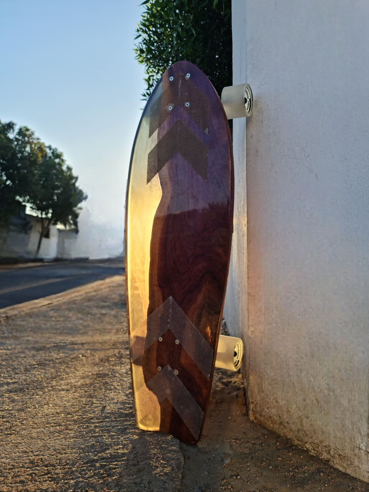 Chevron resin longboard leaning against a white wall at sunset on a quiet street