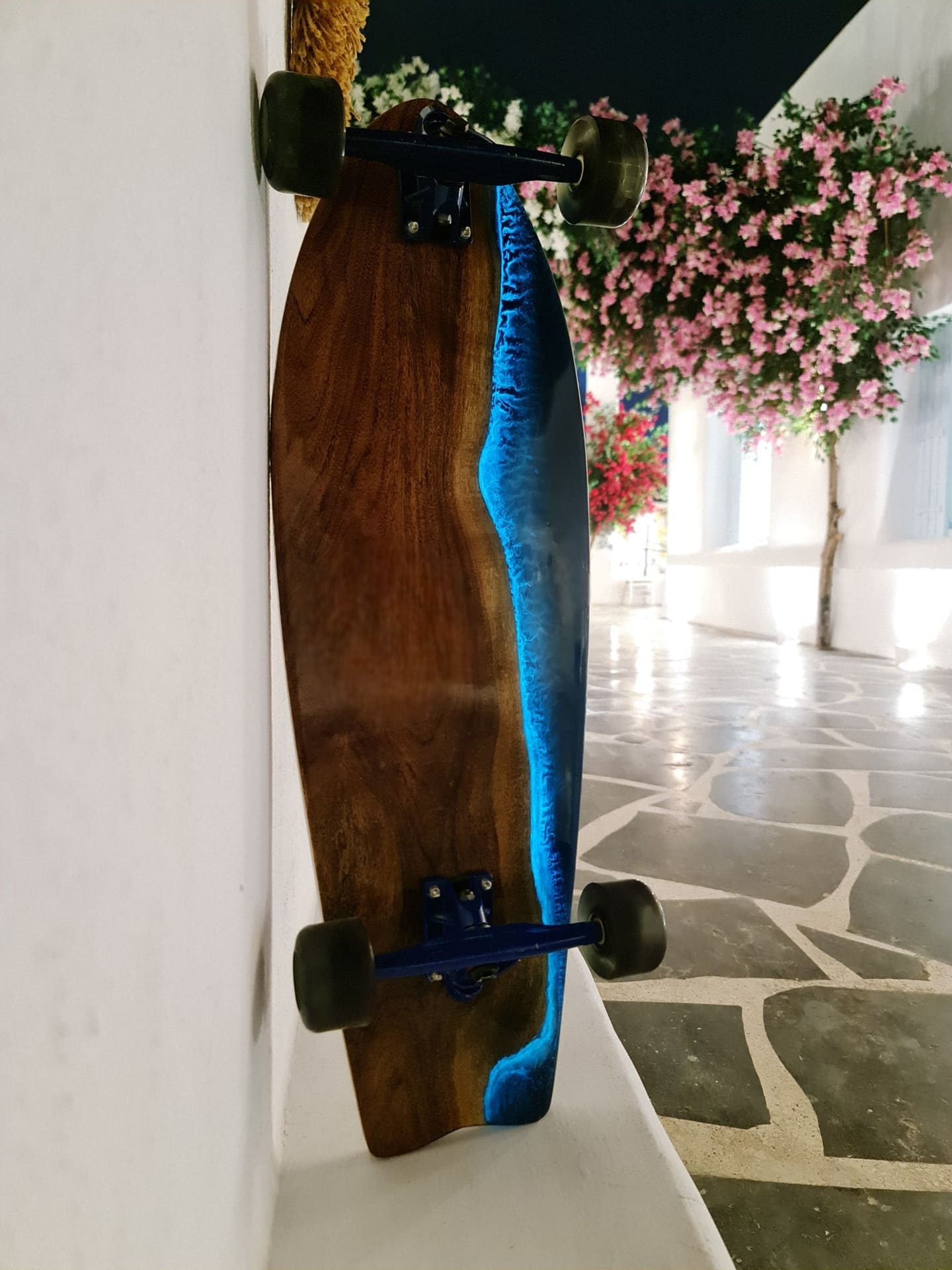 One of None resin longboard photographed in a white studio walkway with flowers