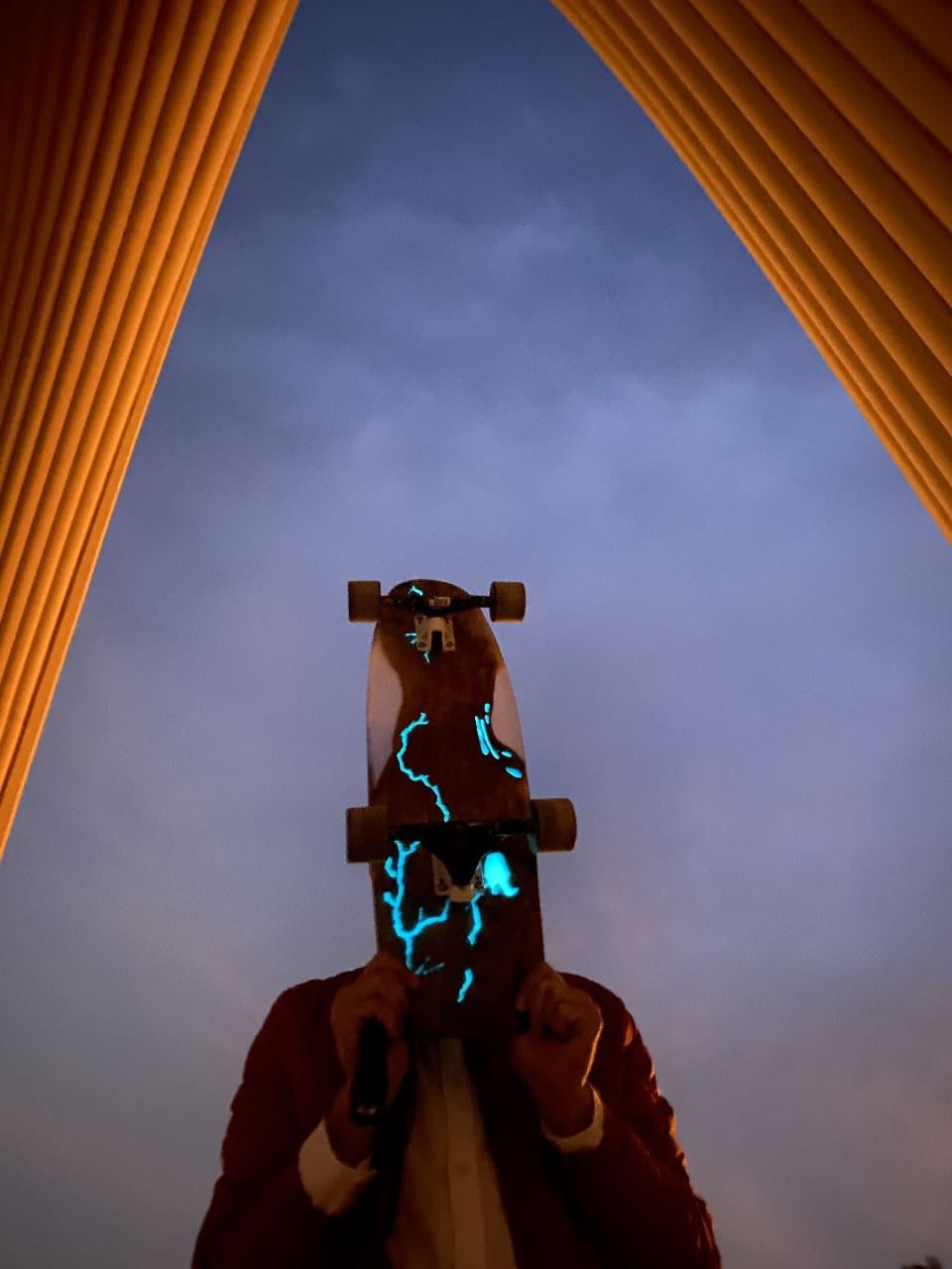 Glow Current longboard glowing cyan resin held up between architectural arches at dusk